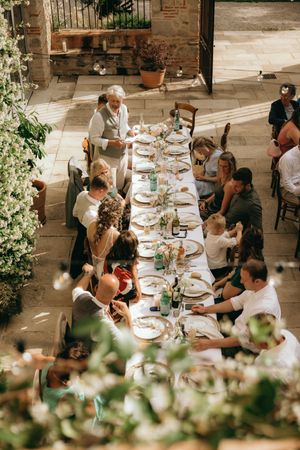 Guests enjoying a wedding reception meal at long tables in a rustic outdoor setting.