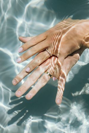 Close-up of hands with wedding rings underwater creating rippling reflections.