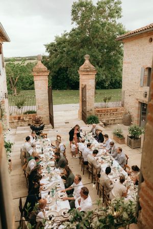 Wedding guests dining at elegant outdoor tables surrounded by stone pillars and greenery.