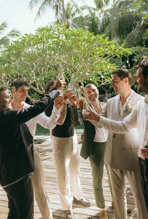 Wedding party in light colored suits toasting and celebrating outdoors.