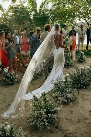 Bridesmaids in flowing white dresses walking through a tropical garden setting.