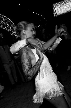 Dancers in fringe dresses twirling on a dark dance floor at a wedding reception.