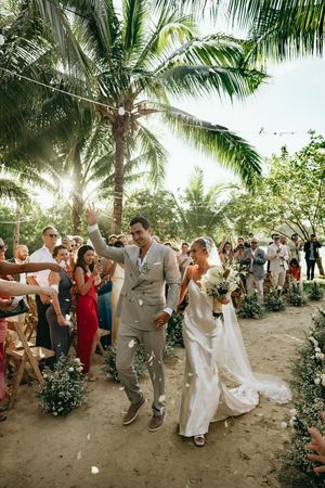 Joyful wedding celebration with guests dancing on a sandy path lined with palm trees.