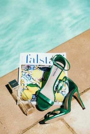 Green high heel shoes and fashion magazines arranged by a swimming pool.