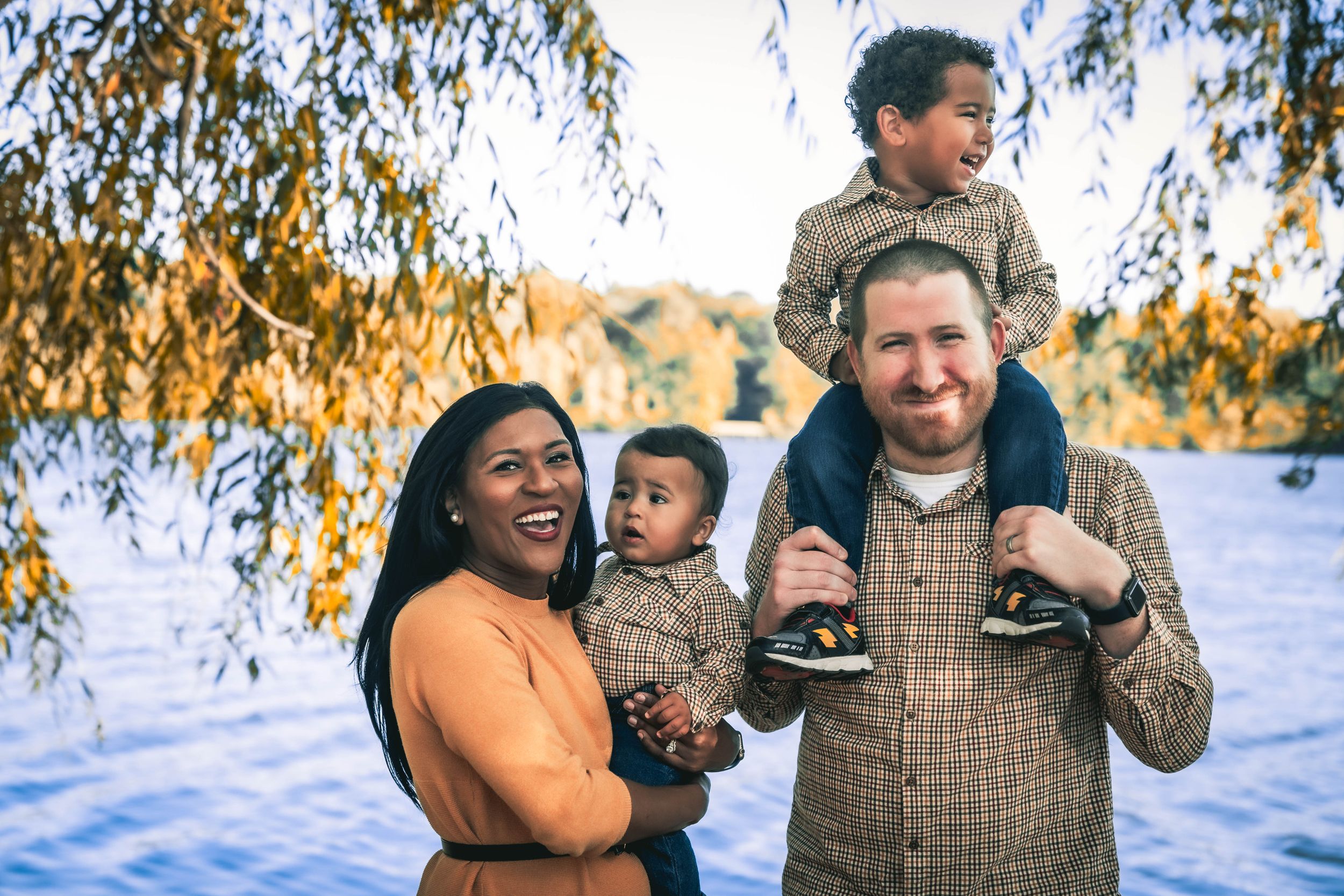 A family of four smiling in front of the water in Oak Grove Lake Park in Chesapeake Virginia