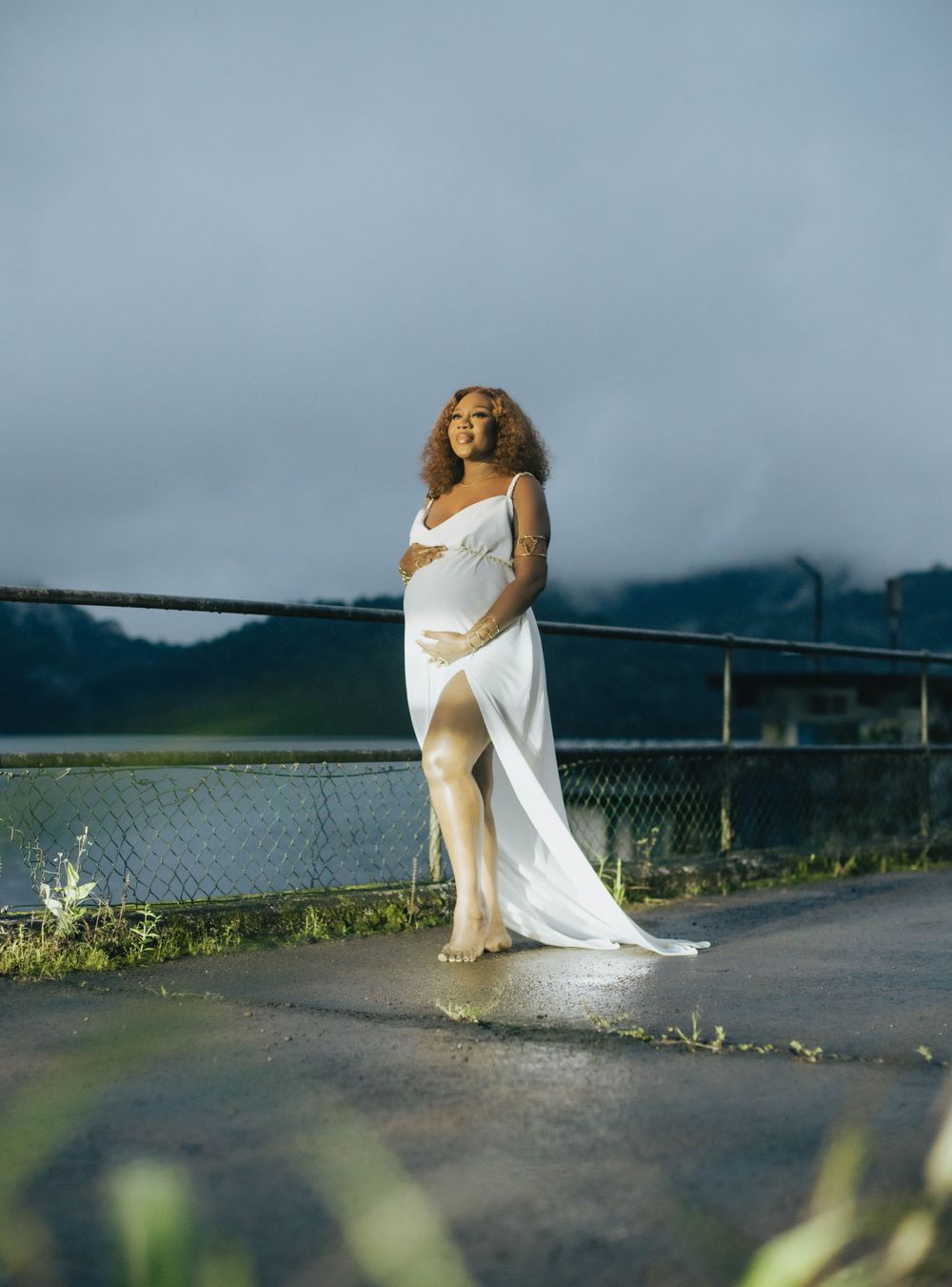 Ethereal maternity photo with flowing white dress against moody sky.