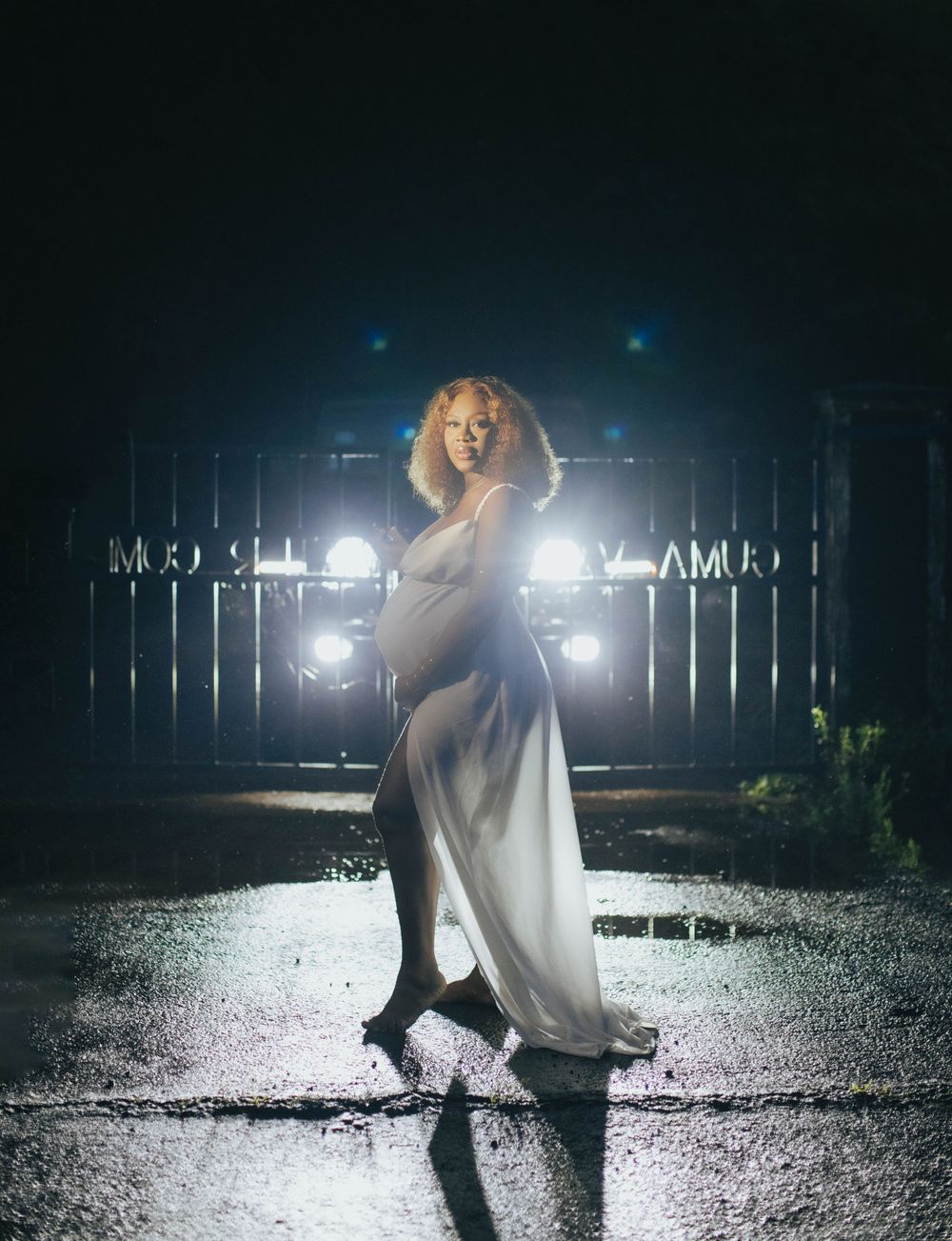 Dramatic nighttime maternity portrait with backlighting and flowing white dress.