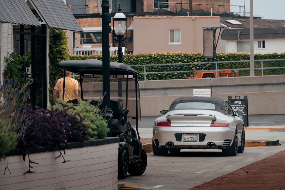 Silver Porsche 911 Turbo convertible parked near a upscale restaurant entrance on a cloudy day.