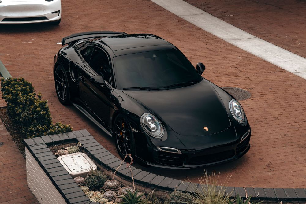 Black Porsche 911 Turbo S shot from above parked on brick pavers near desert landscaping.