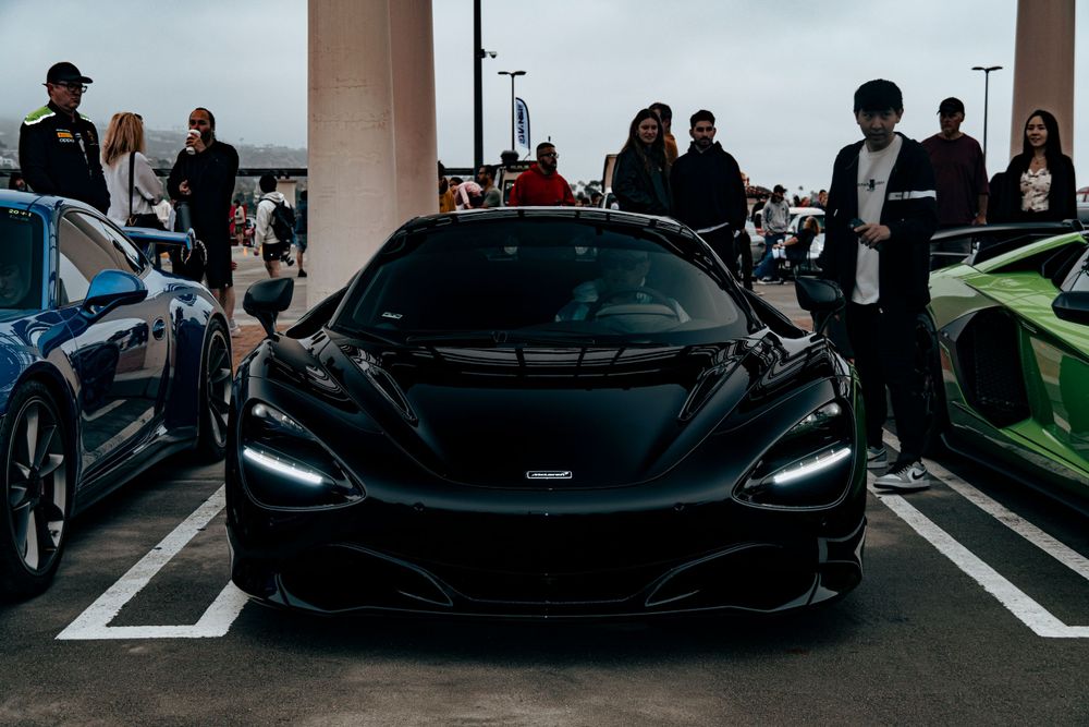 Black McLaren supercar displayed at an outdoor exotic car show surrounded by spectators.