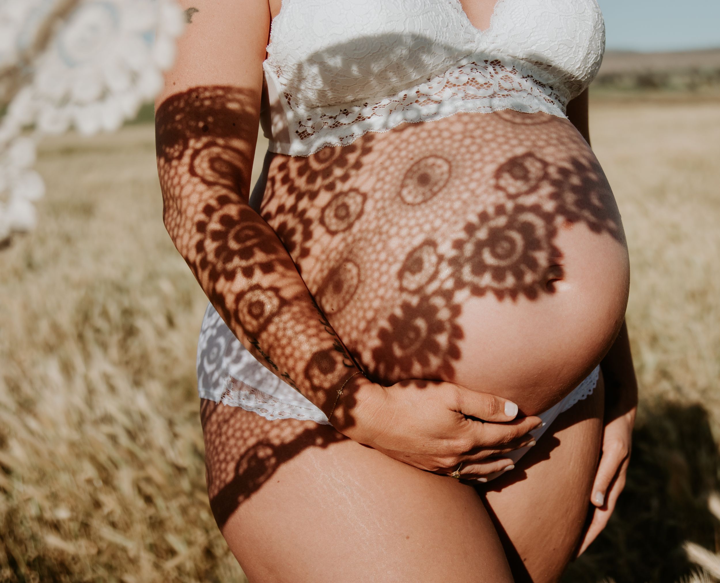 A pregnant belly, hand cradling with lace bra and shadow