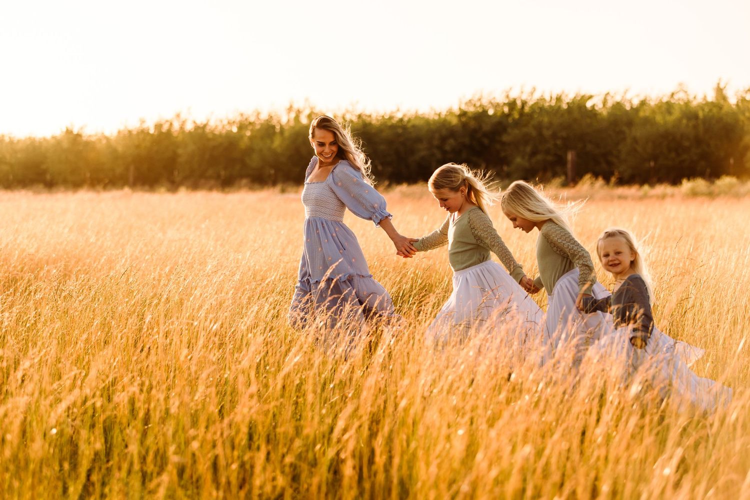 Group in flowing white dresses walks together through sun-lit field at golden hour.