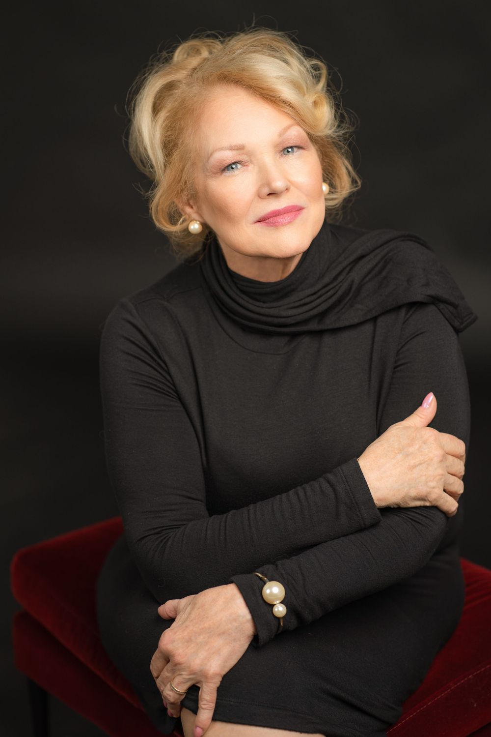 Professional portrait of a woman in a black turtleneck sweater seated against dark background.