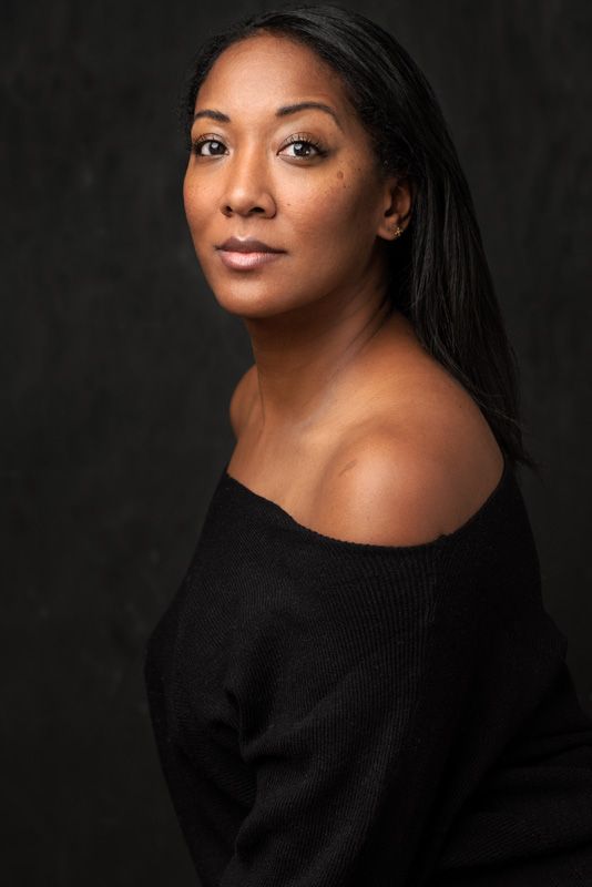 Studio portrait showing off-shoulder black sweater against dark background.
