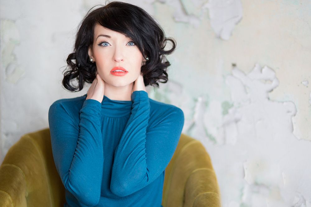 Portrait of woman in teal turtleneck sweater posed on yellow chair.