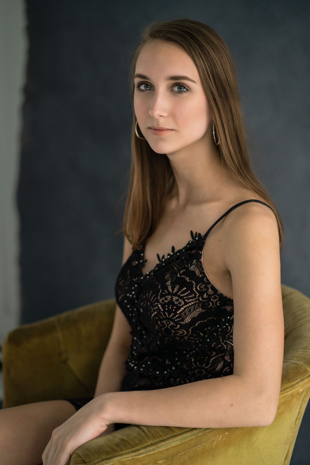 Elegant portrait in black lace dress seated on velvet chair.