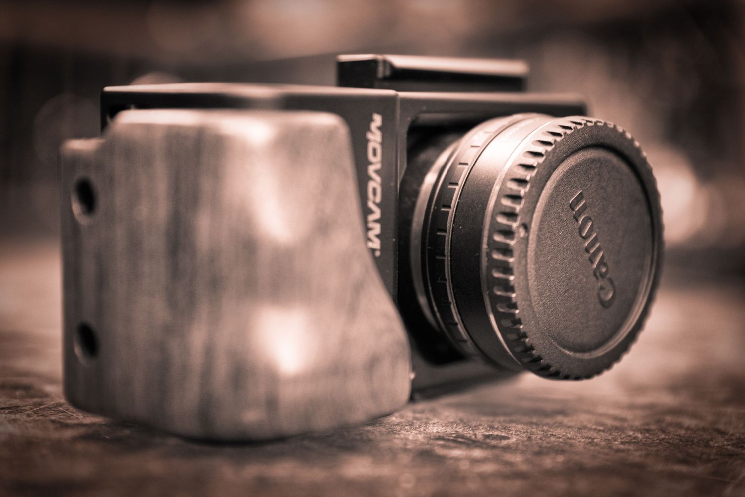 Old vintage camera and lens cap on wooden surface in sepia tones with shallow depth of field.