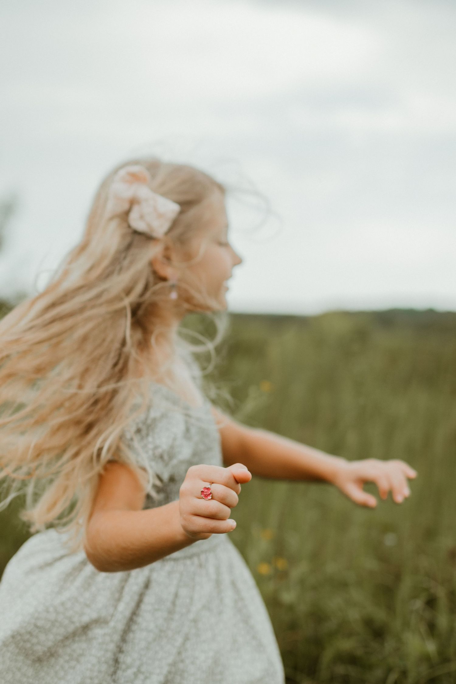 Young girl in a gray dress spins joyfully in a meadow with her blonde hair flowing in the wind. Spartanburg South Carolina