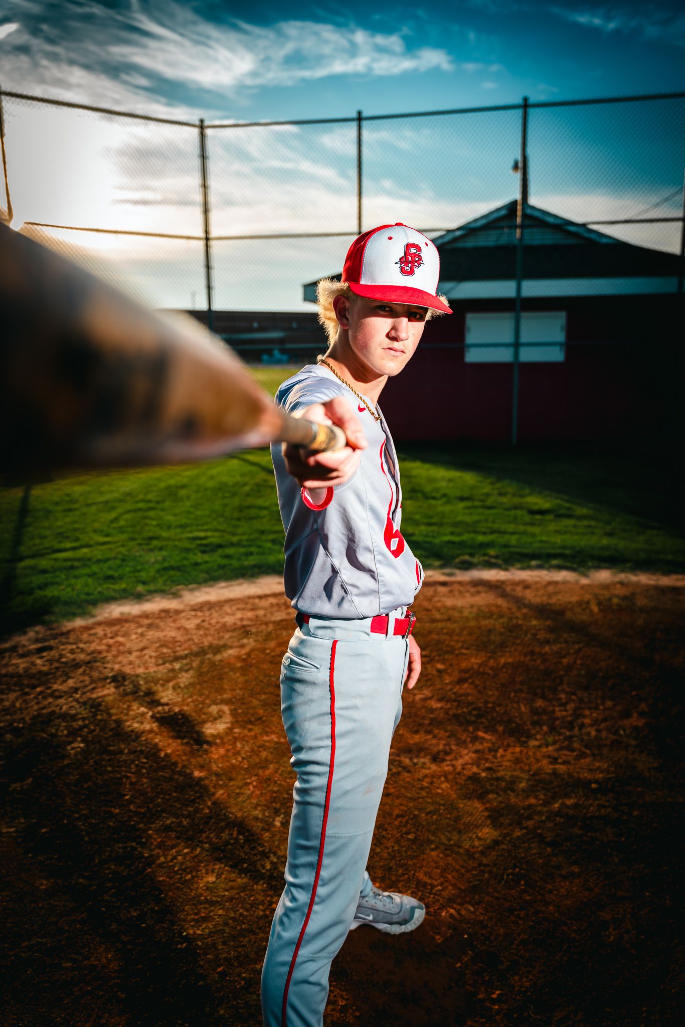 Baseball player in uniform poses dramatically against blue sky on baseball field.