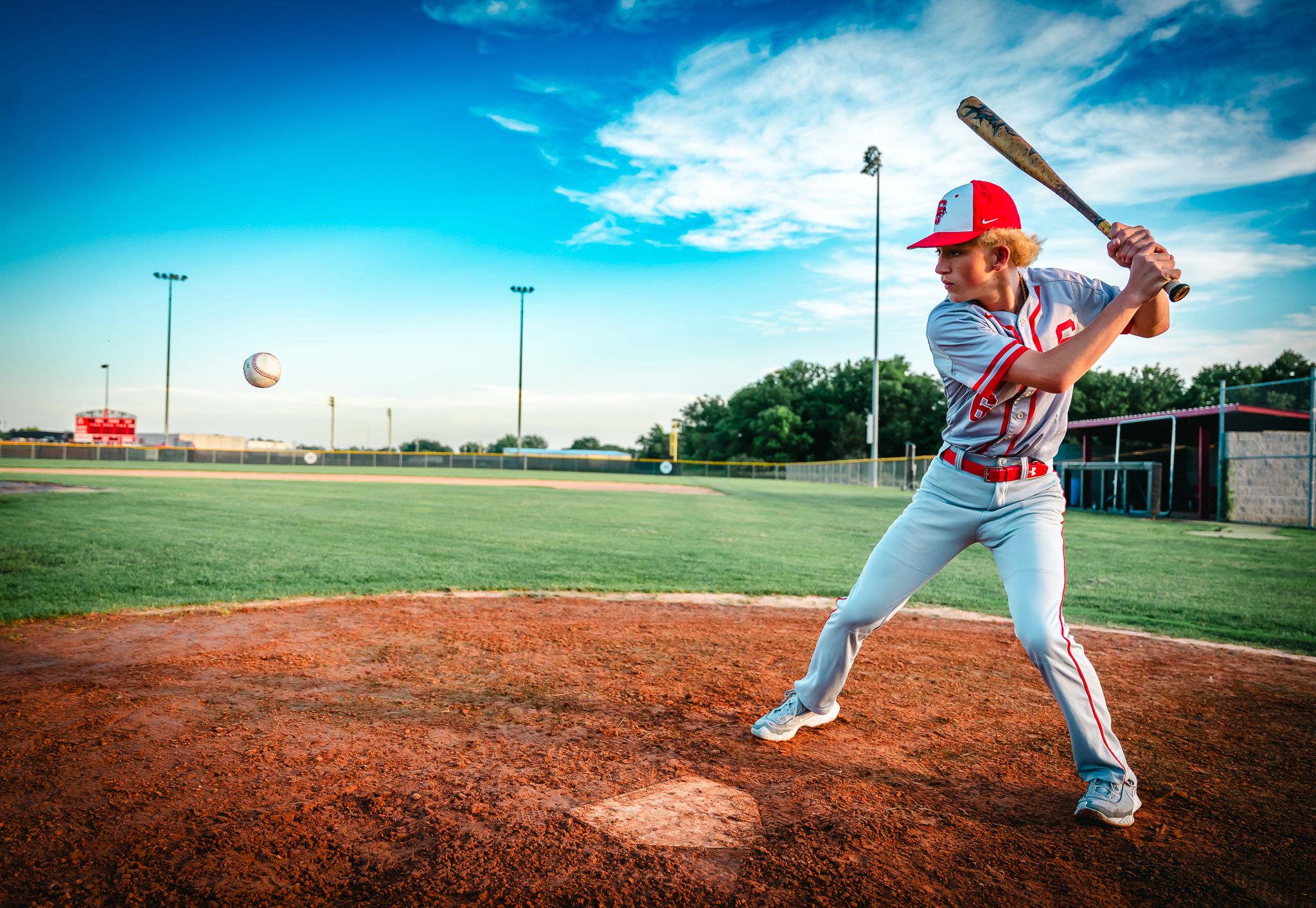 Baseball player in white uniform takes batting stance on pitcher's mound under bright blue sky.