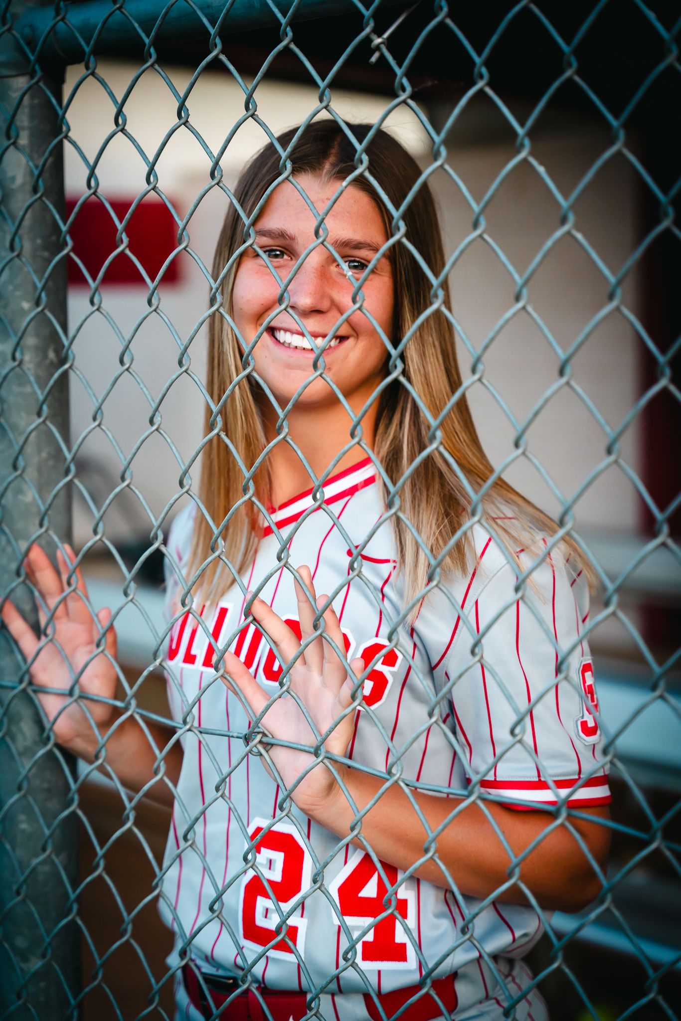 Baseball player in pinstriped uniform poses behind chain link fence at sports field.