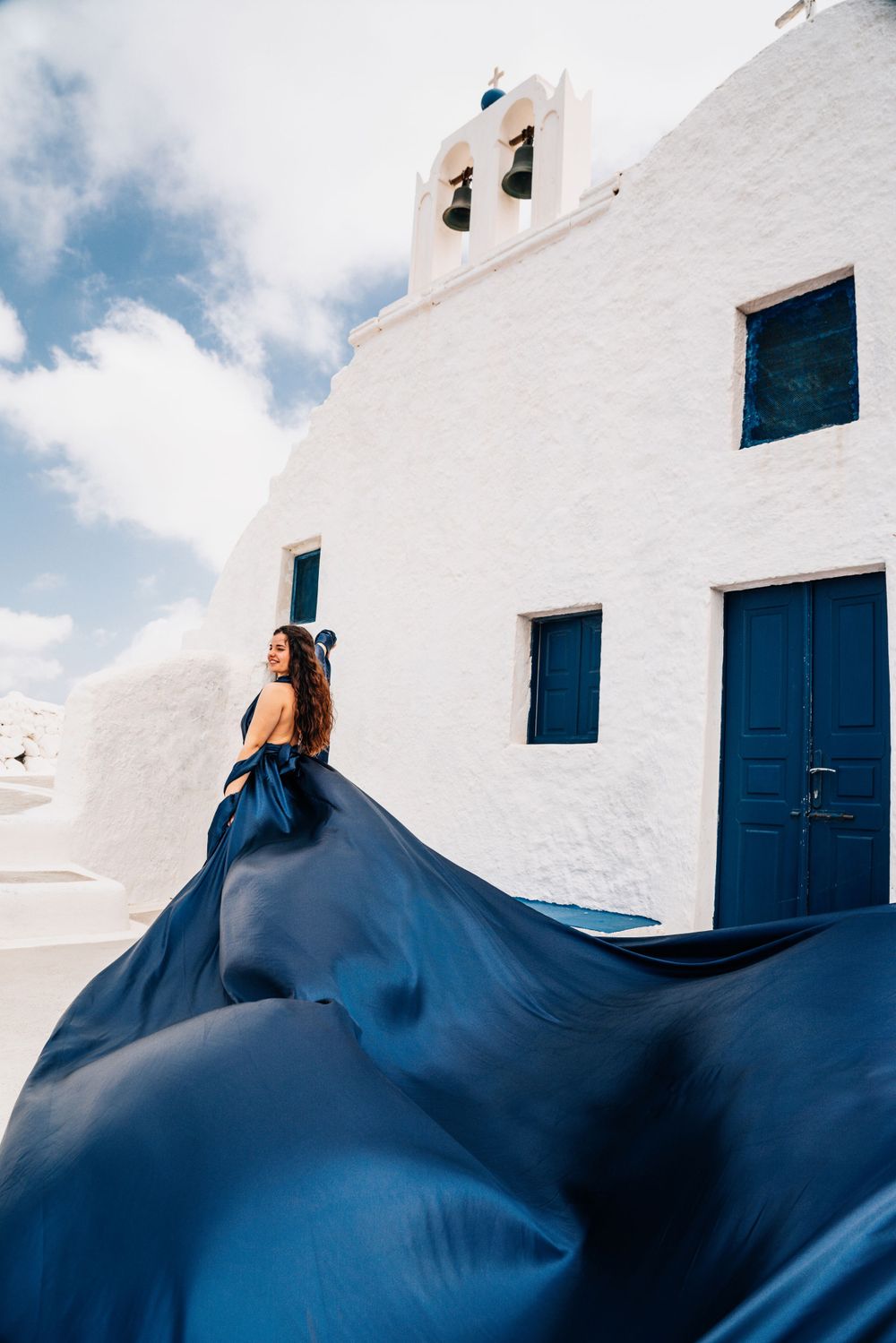 Dark blue fabric billows dramatically against whitewashed church with blue accents.