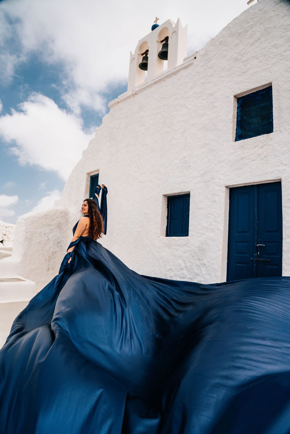 Navy blue flowing dress creates dramatic silhouette against white Greek church facade.