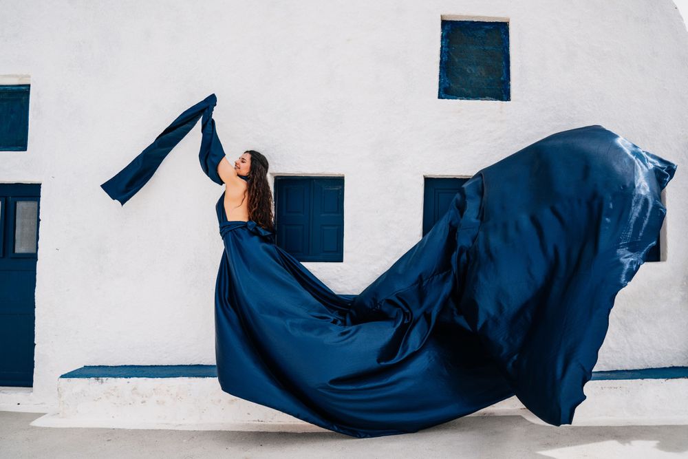 Flowing navy blue fabric billows dramatically against a white Mediterranean building with blue windows.