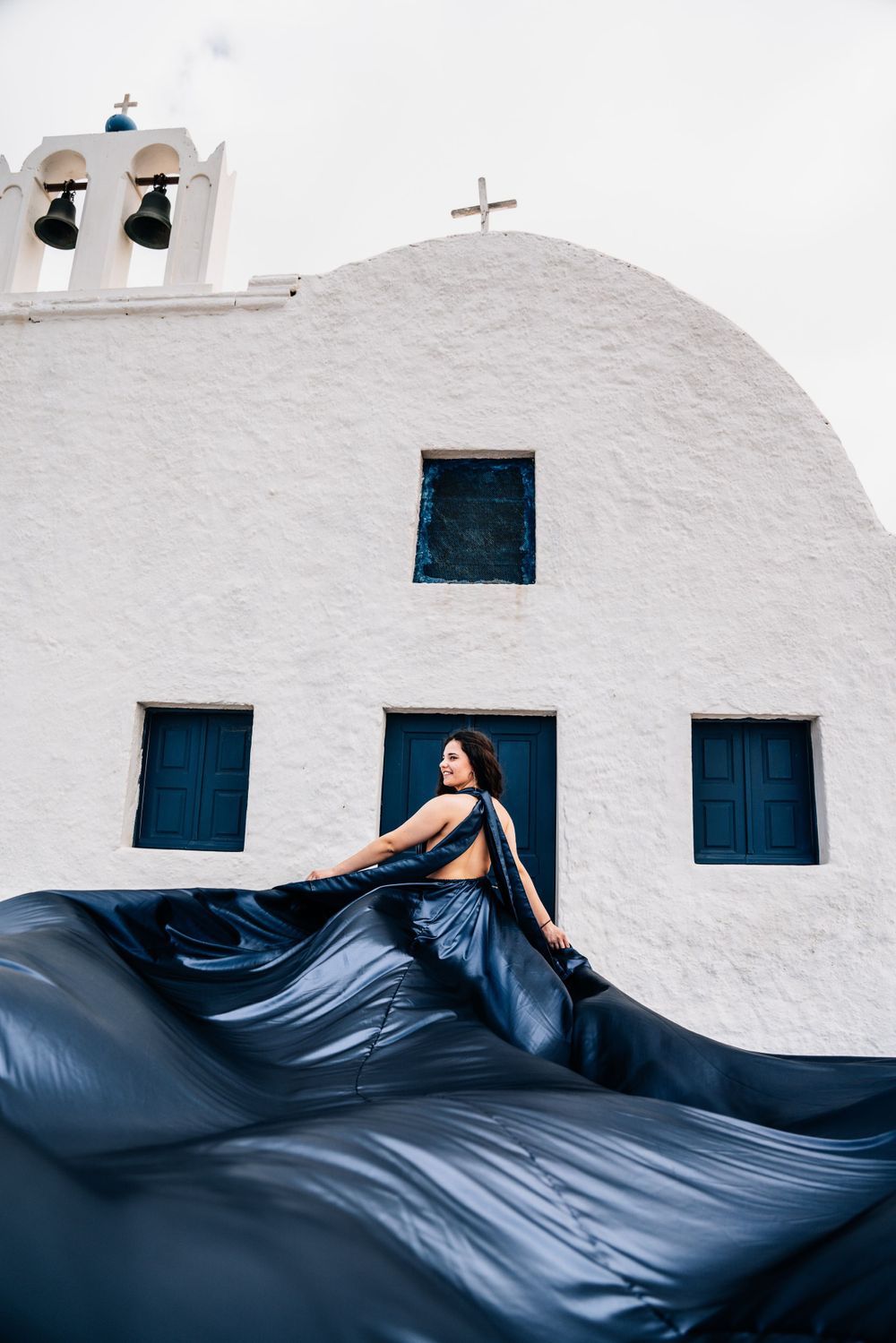 Dark blue flowing fabric contrasts against white church with bell tower and blue windows.