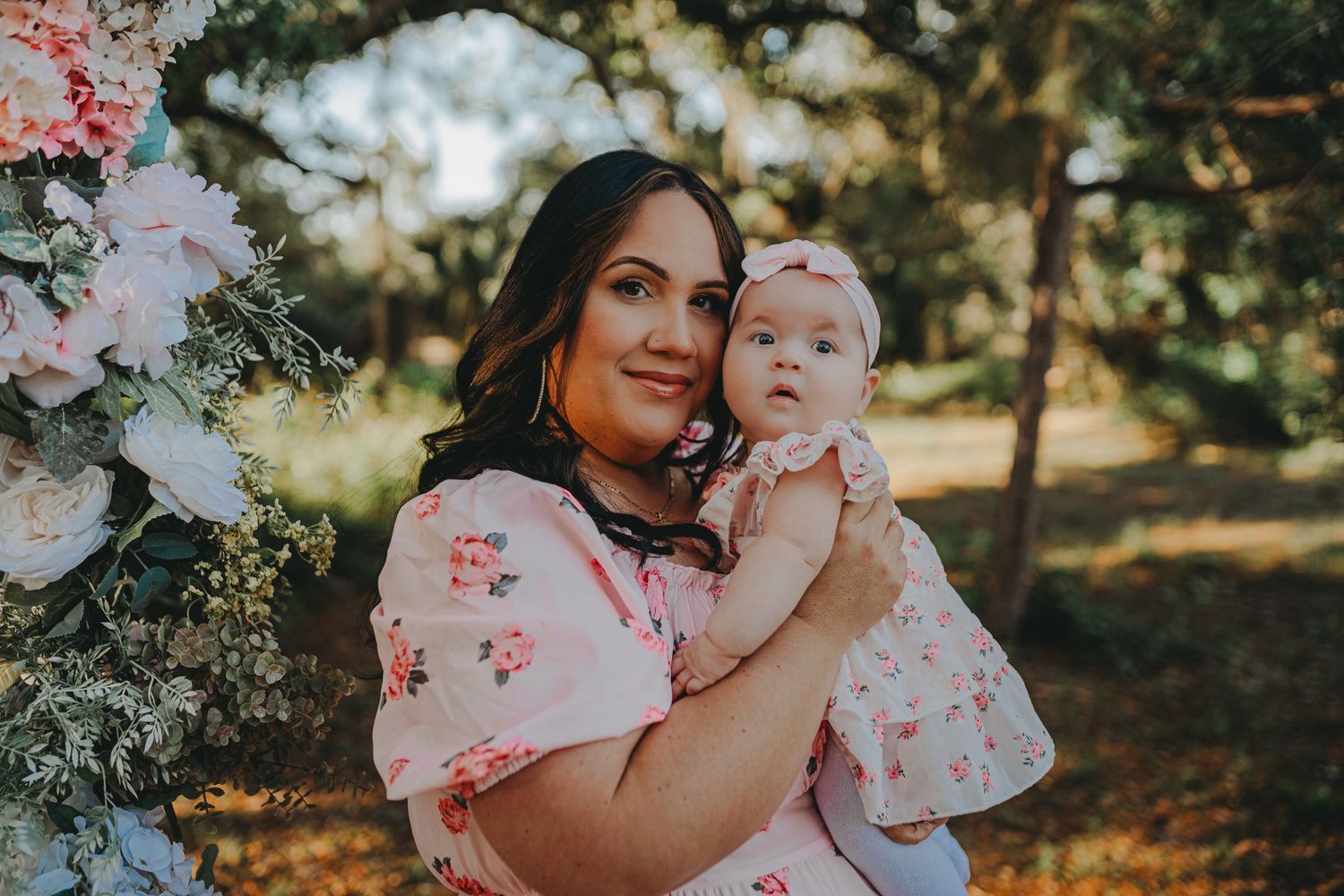 Mother and child portrait under a floral arch with soft natural lighting.