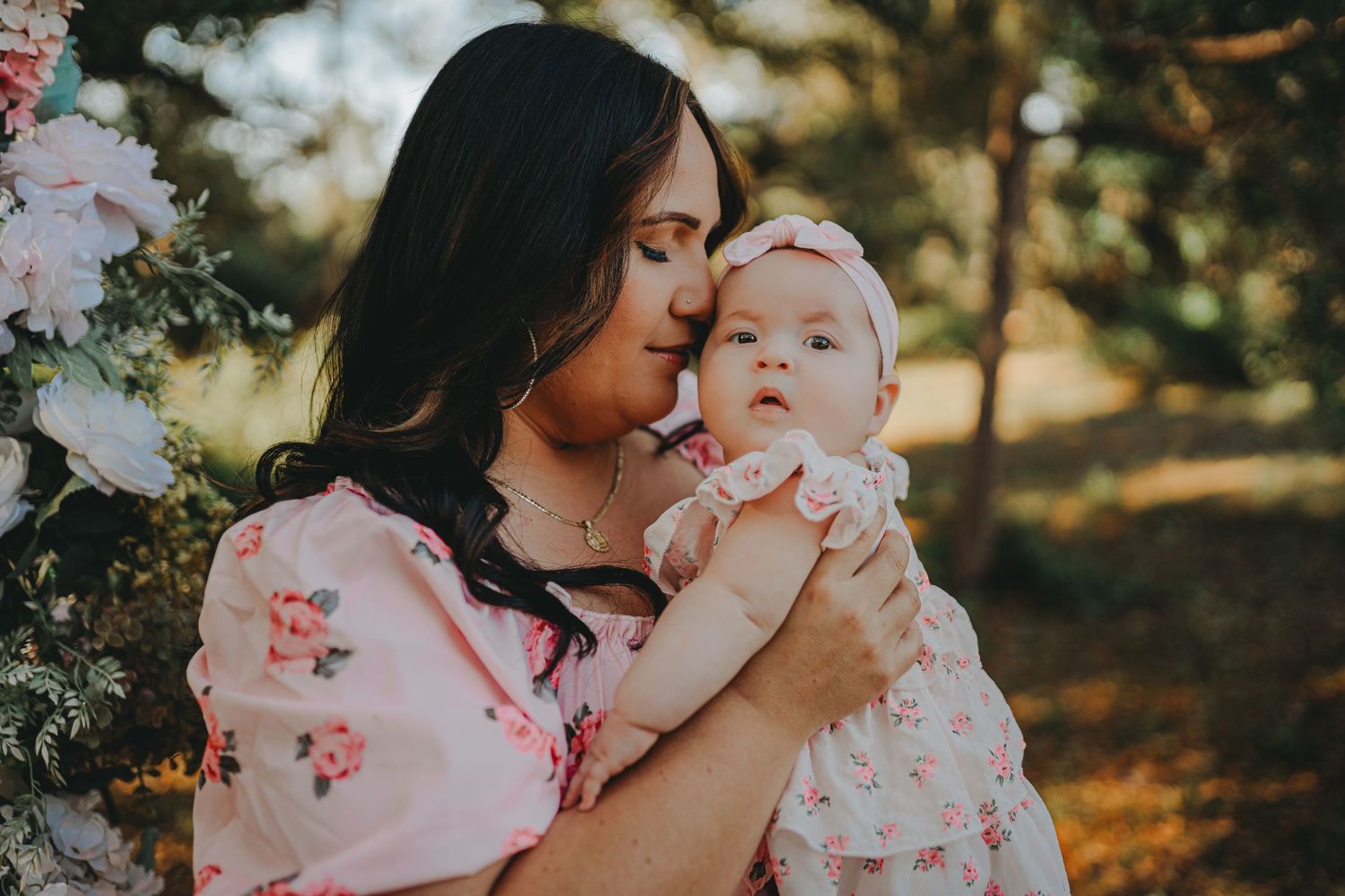 Tender moment between mother and baby under floral decorations in outdoor setting.