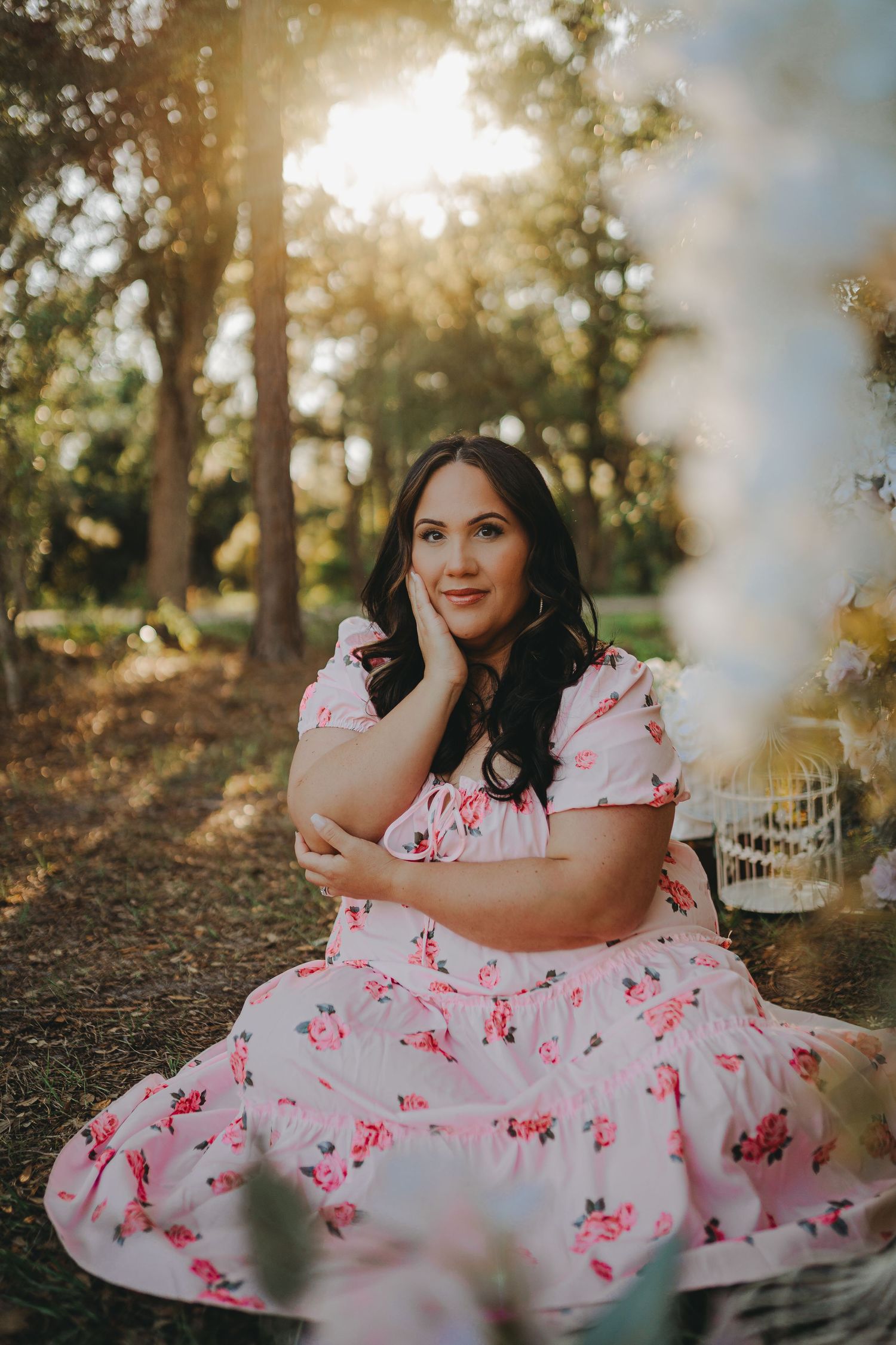 Portrait in pink floral dress with dreamy sunlit forest backdrop and decorative elements.