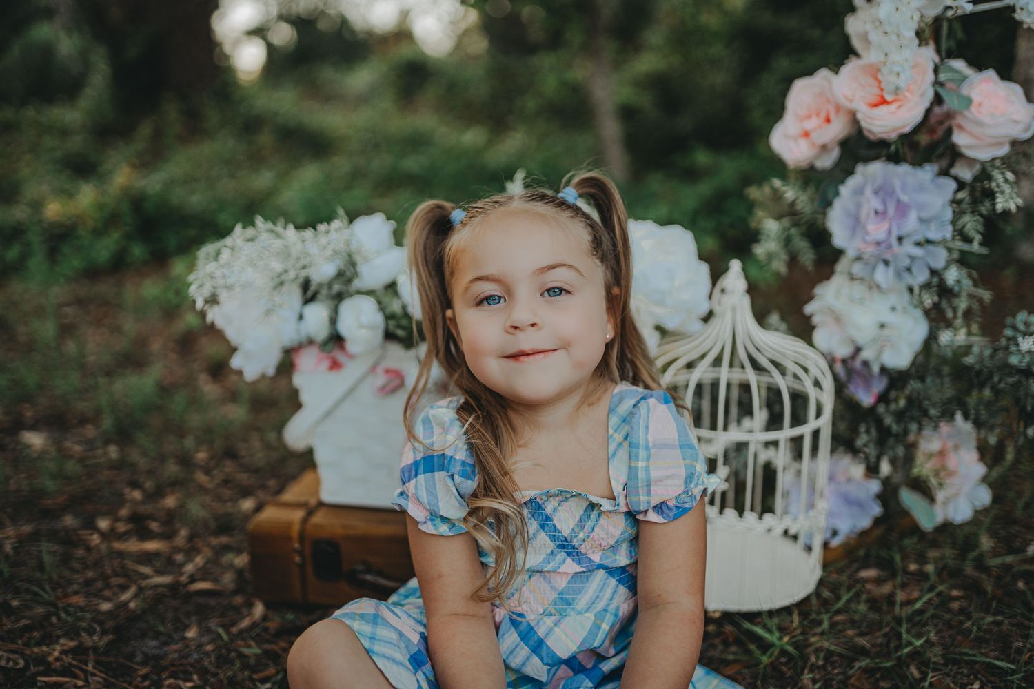 A vintage-styled portrait setup with decorative birdcages and florals in a garden setting.