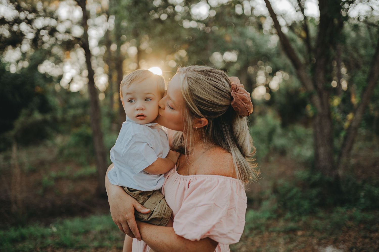 An intimate outdoor family moment captured during golden hour in a wooded setting.