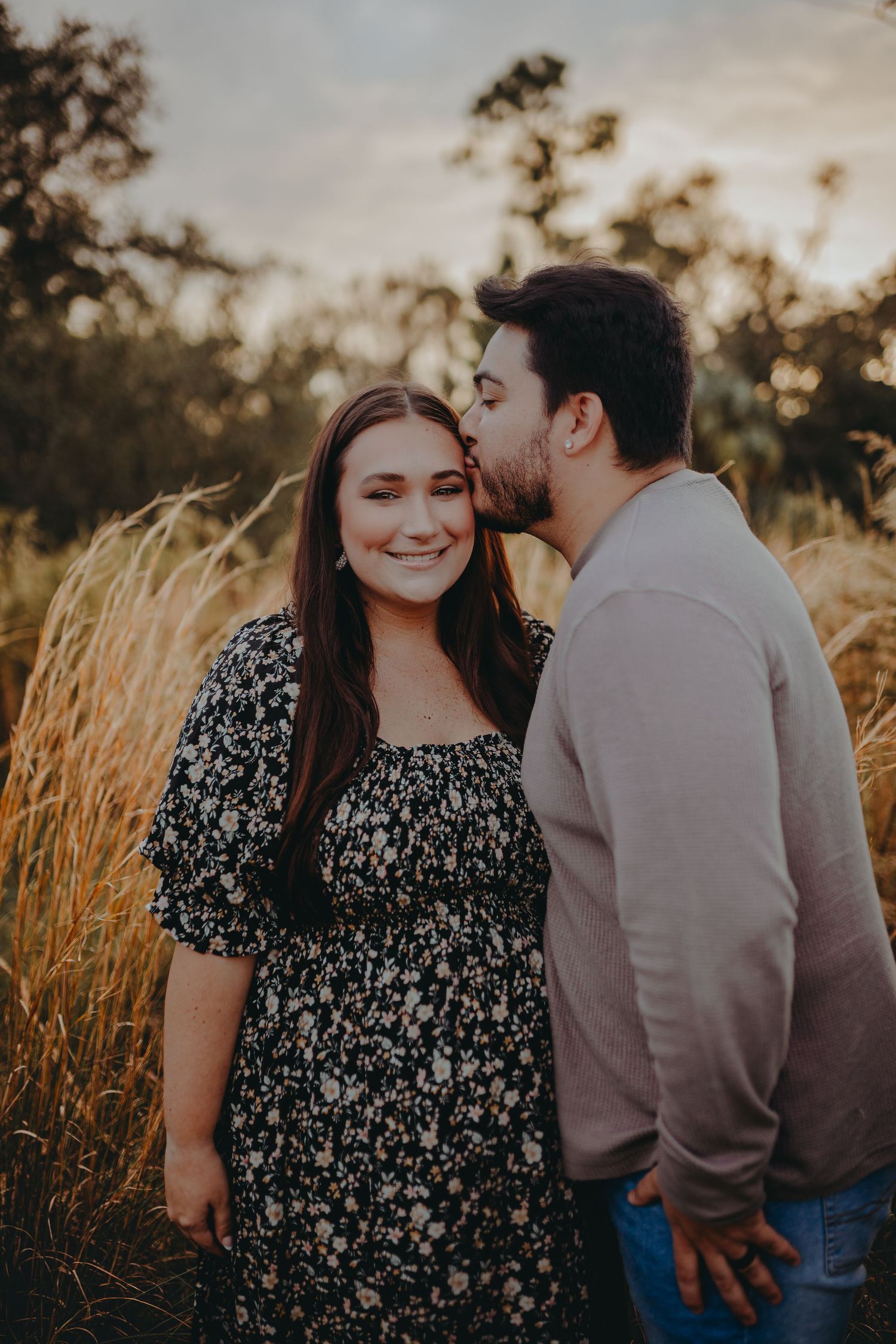 Intimate couple portrait in tall golden grass during sunset with soft lighting.