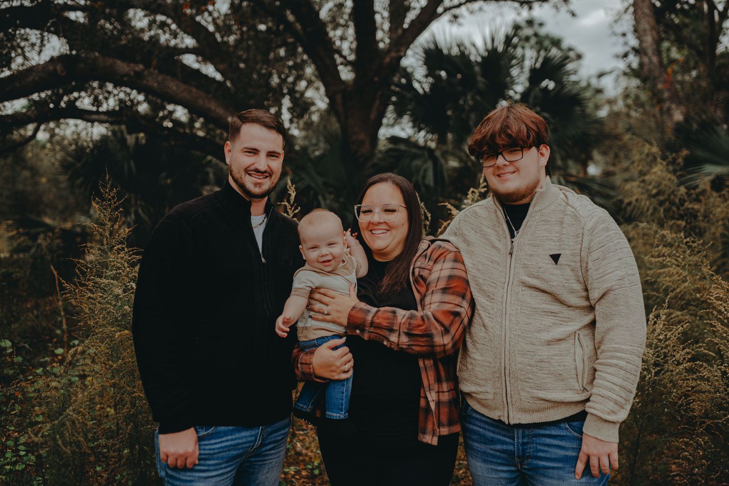 Family portrait captured outdoors in autumn with tree branches framing the scene at sunset.