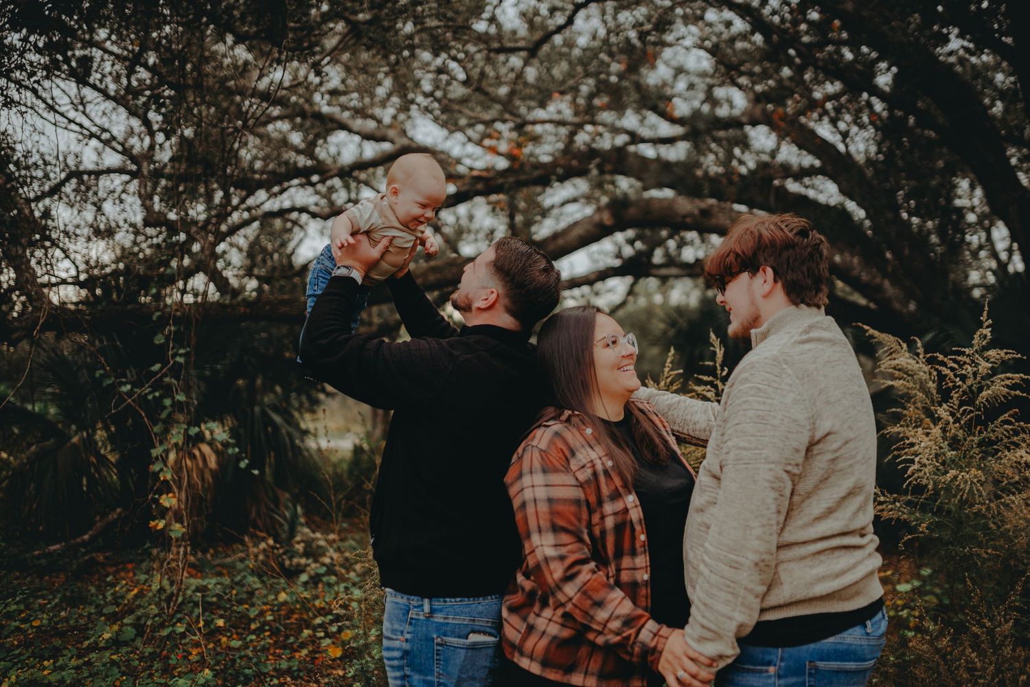 Candid moment of family interaction during an outdoor photo session with dramatic tree backdrop.