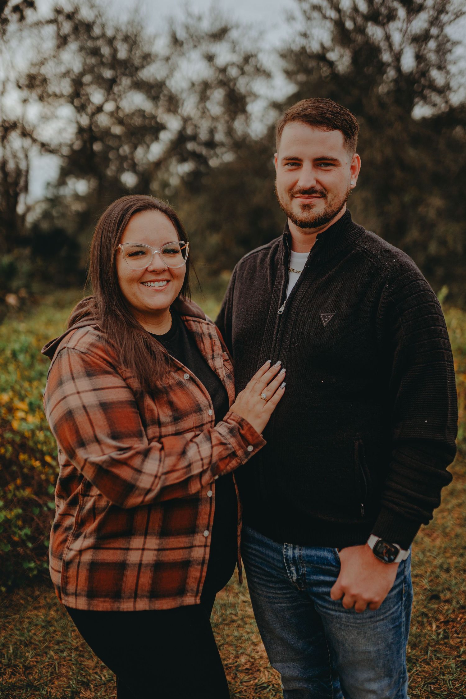 Couple in casual autumn attire posing for outdoor portrait with natural fall scenery.