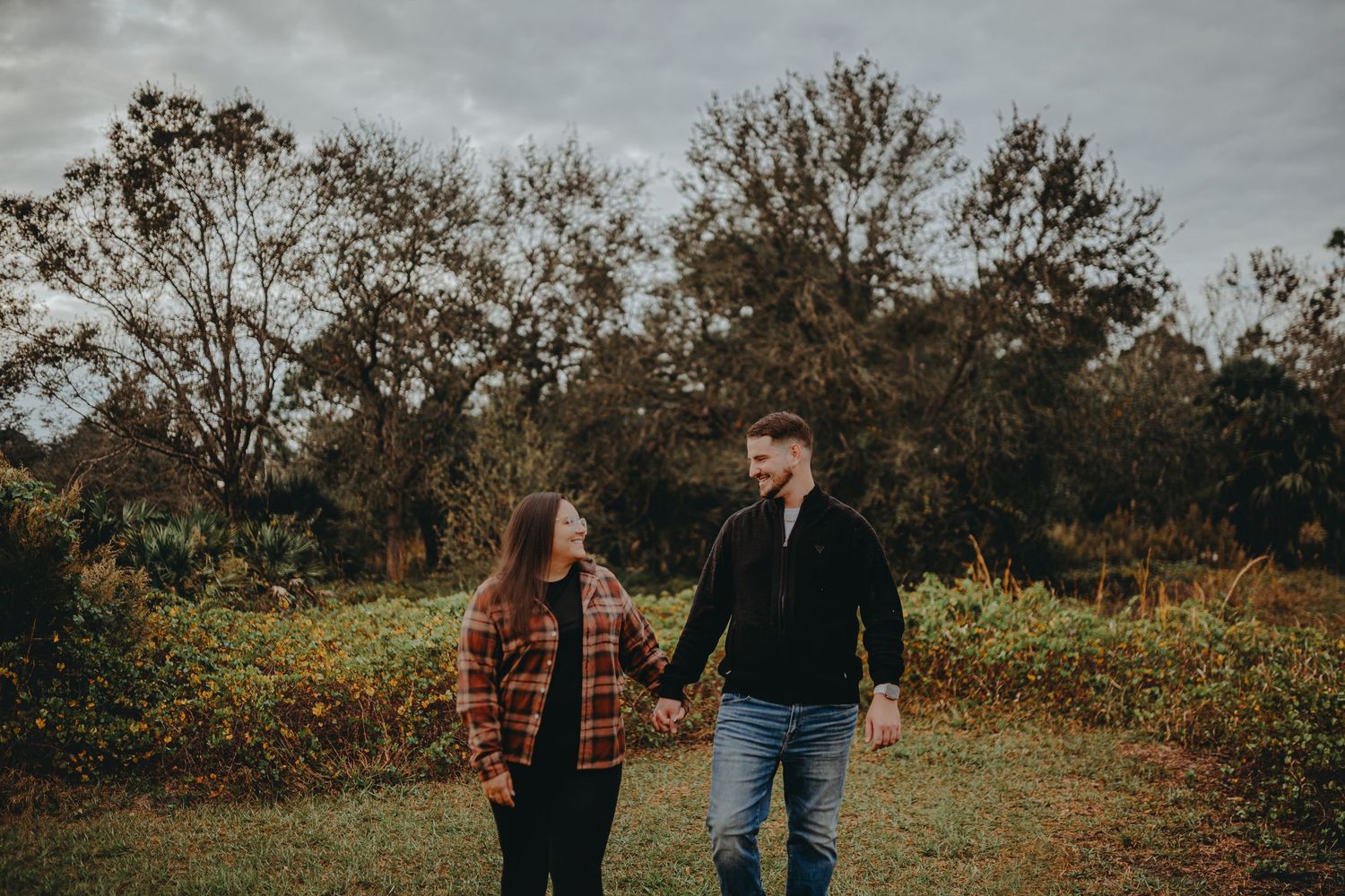 Couple walking together through scenic fall landscape with moody overcast sky.