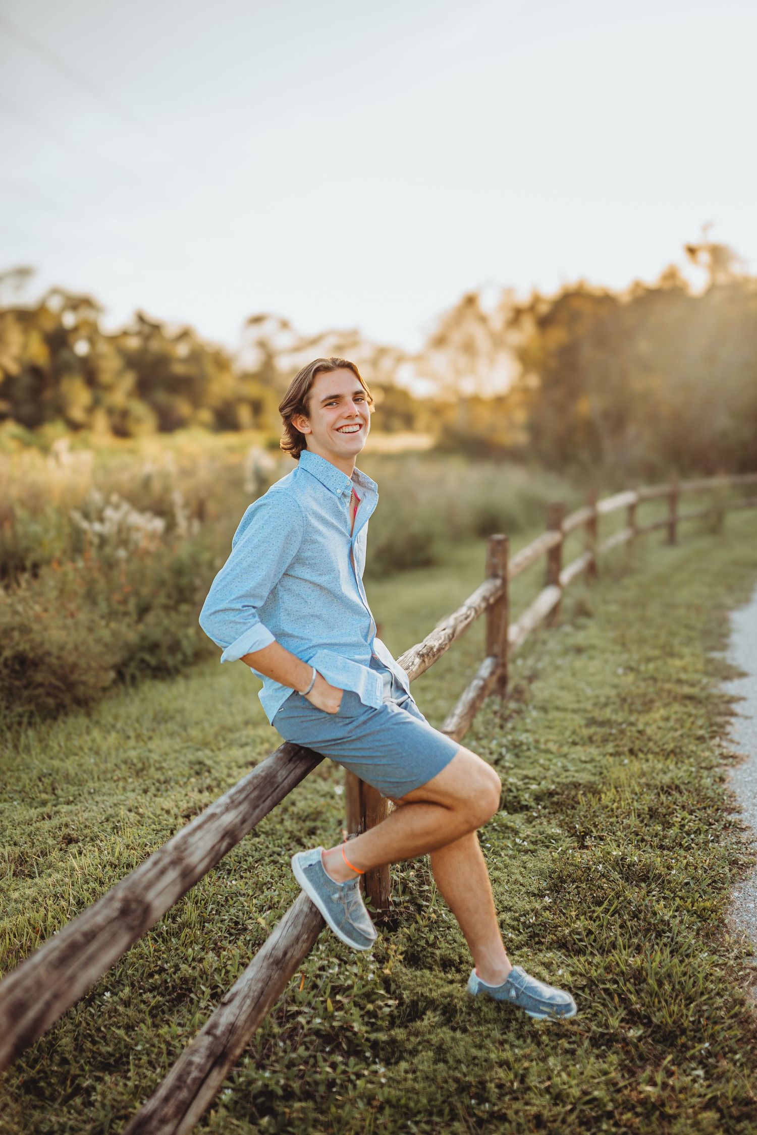 A casual portrait of someone sitting on a wooden fence in summer attire.