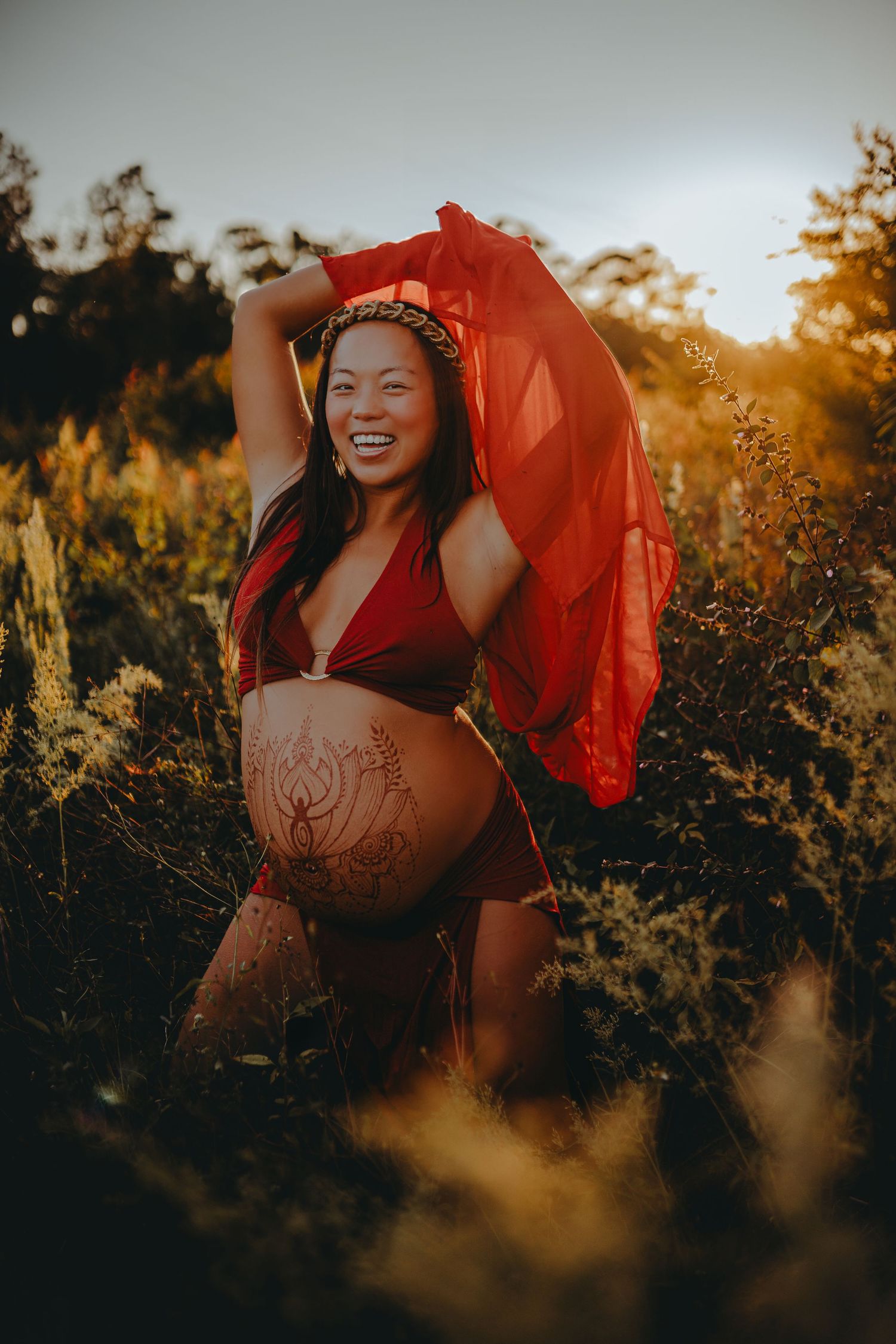 A joyful maternity photo with flowing red fabric in golden sunlight.