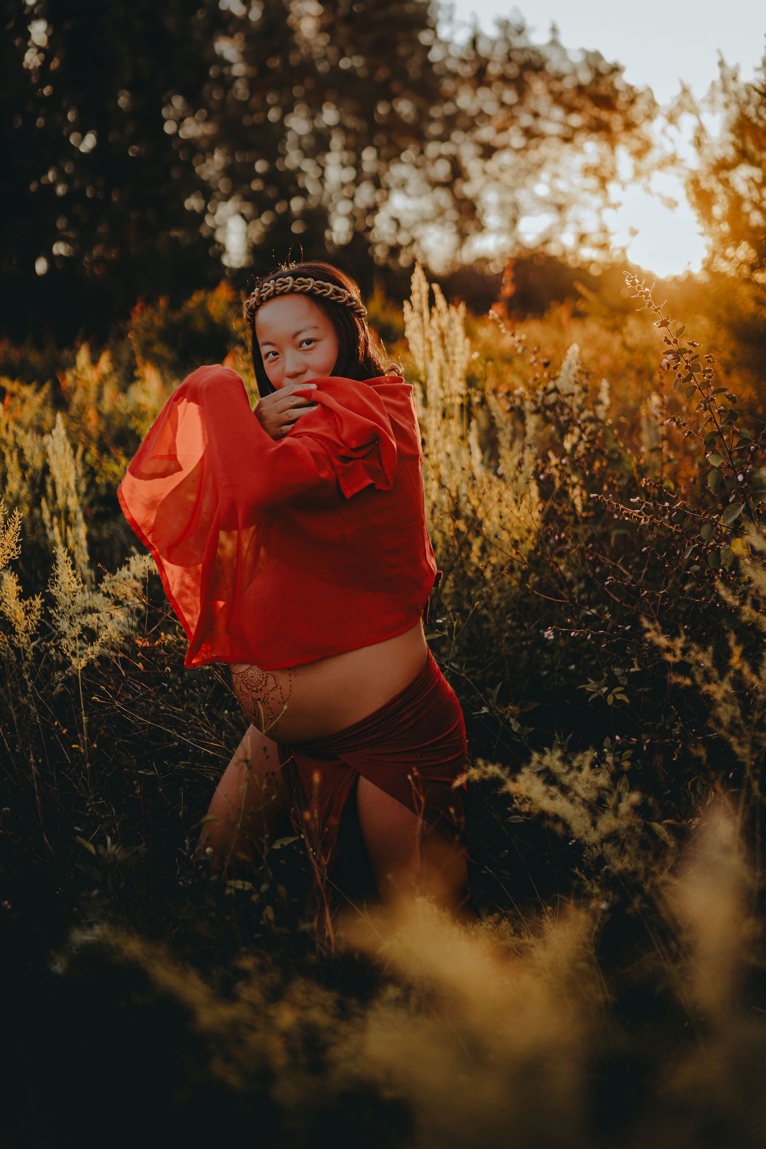A dramatic maternity portrait with red flowing fabric at sunset.