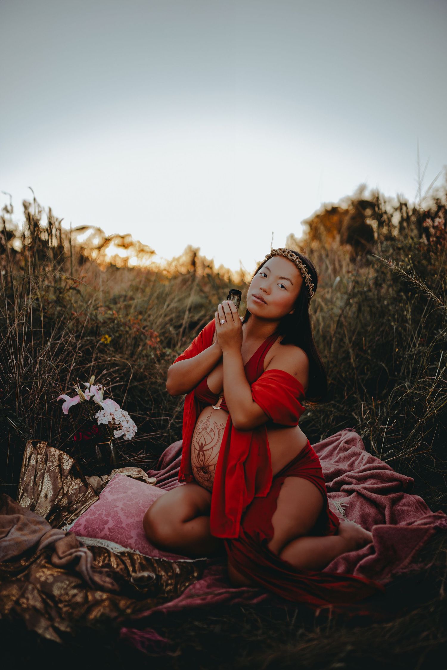 A romantic outdoor portrait featuring a figure in red on a blanket at sunset with delicate flowers.