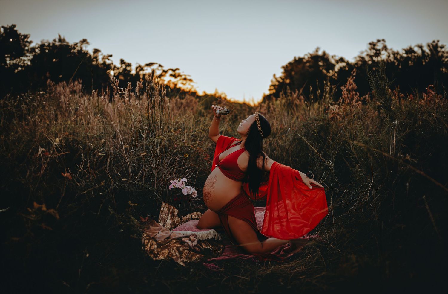 A maternity photo session featuring red fabric in a natural setting at sunset.