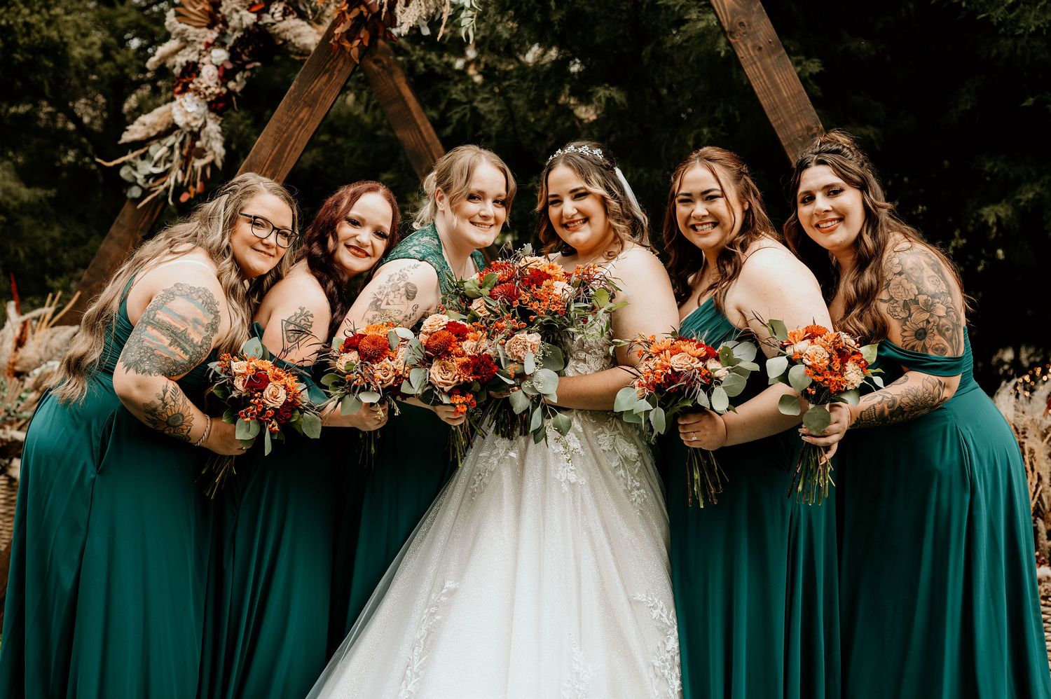 Bride and bridesmaids in front of a rustic wedding arch