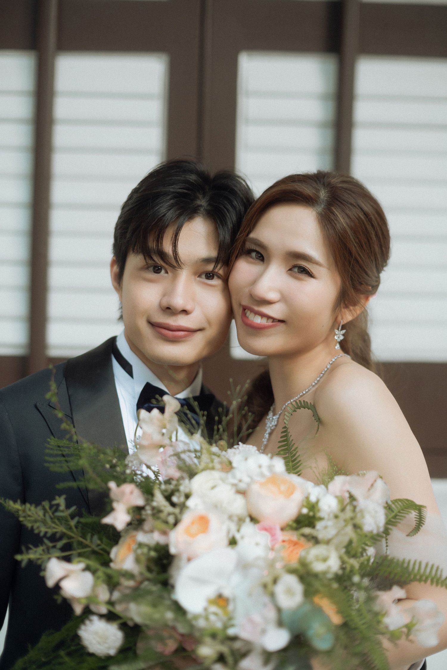 Elegant wedding portrait with a beautiful floral bouquet featuring peach and white blooms.