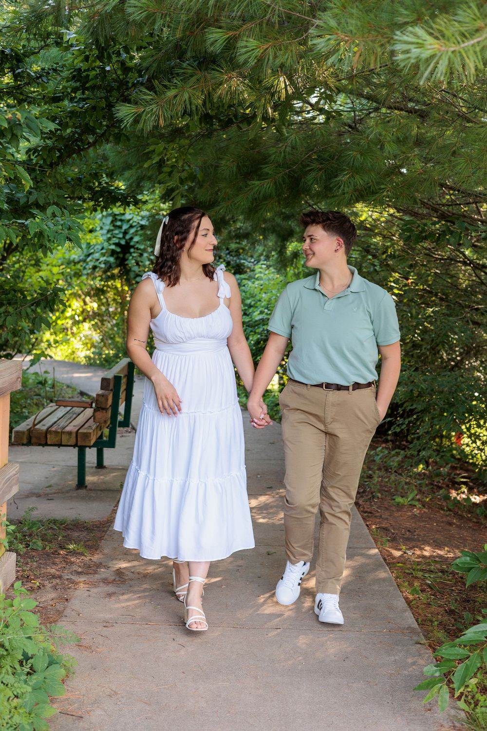 Couple strolls hand in hand along garden path wearing white dress and sage green shirt.