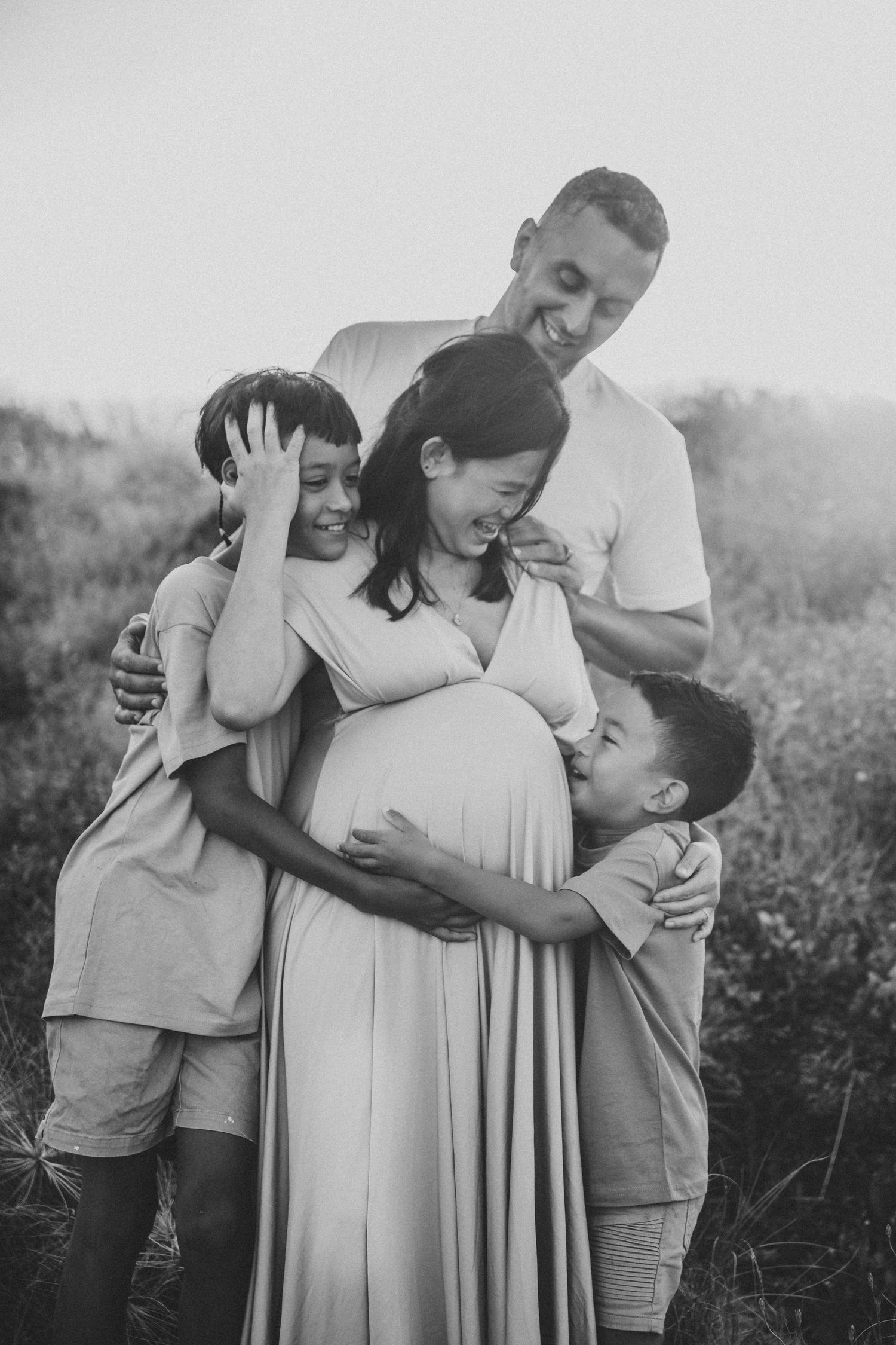 Expecting couple embraces in tall grass during golden hour sunset.