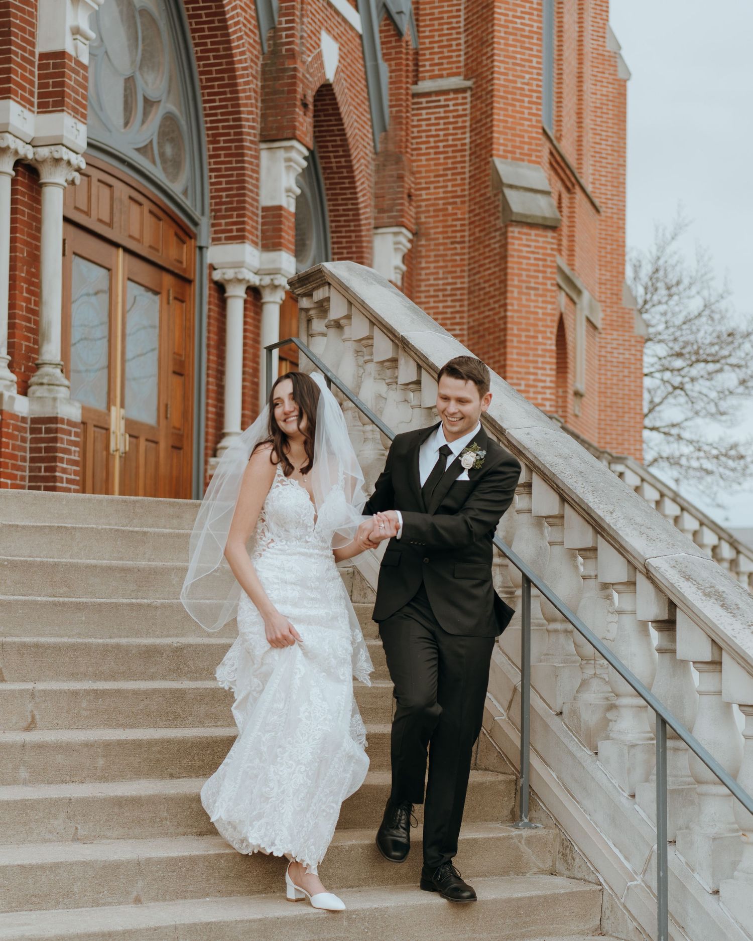 Bride and Groom descending beautiful vintage Catholic Church stairs after wedding ceremony smiling with joy to be newlyweds.