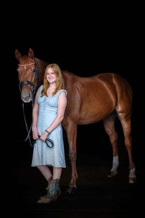 A beautiful chestnut horse stands next to someone in a light blue dress against a dark background in a photo series.